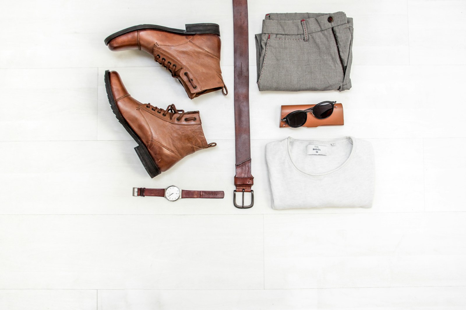 Brown leather boots laid out with a matching belt, watch, sunglasses and clothes